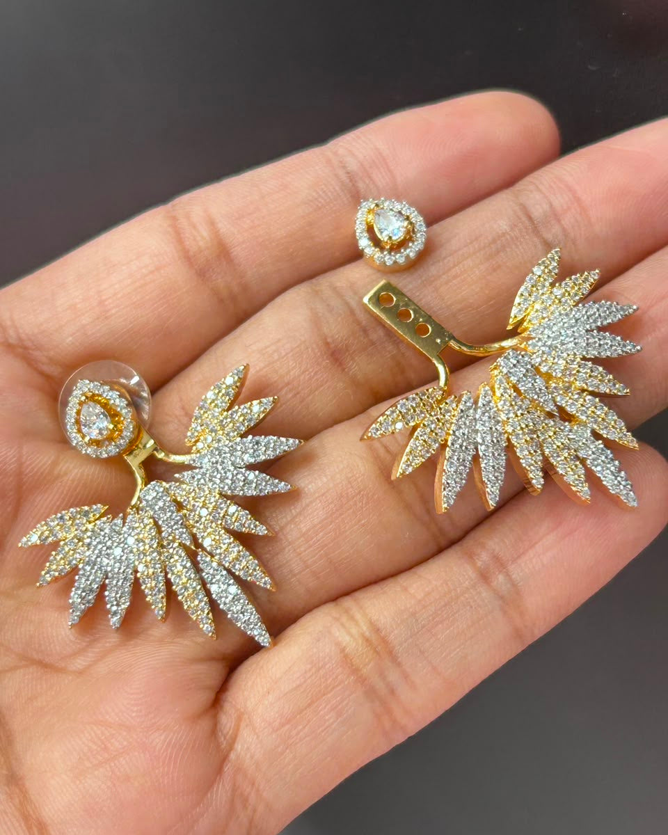 Gold and crystal pavé wing-shaped earrings displayed on a person's hand.