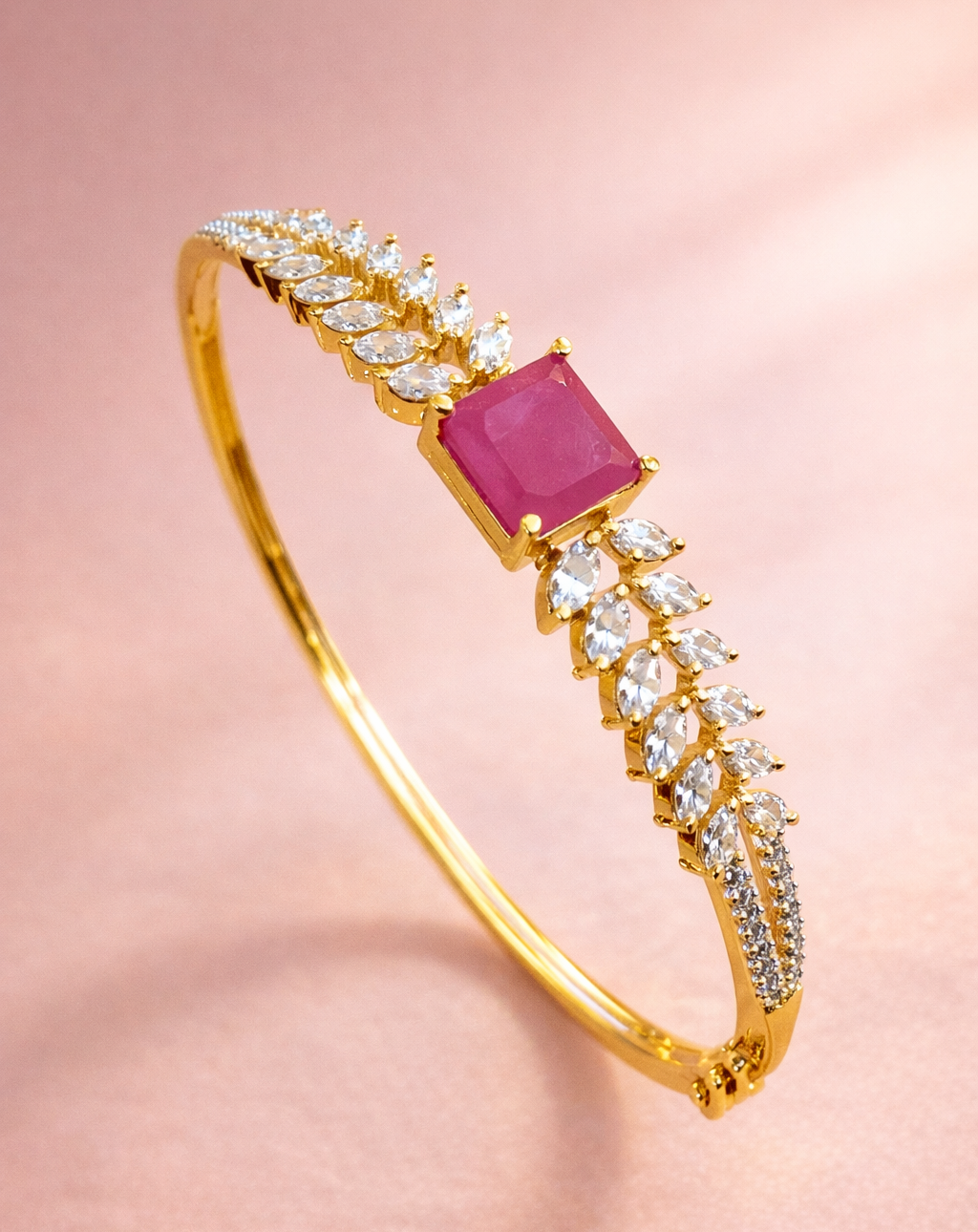 Gold bracelet with a pink gemstone and diamond accents on a pink background