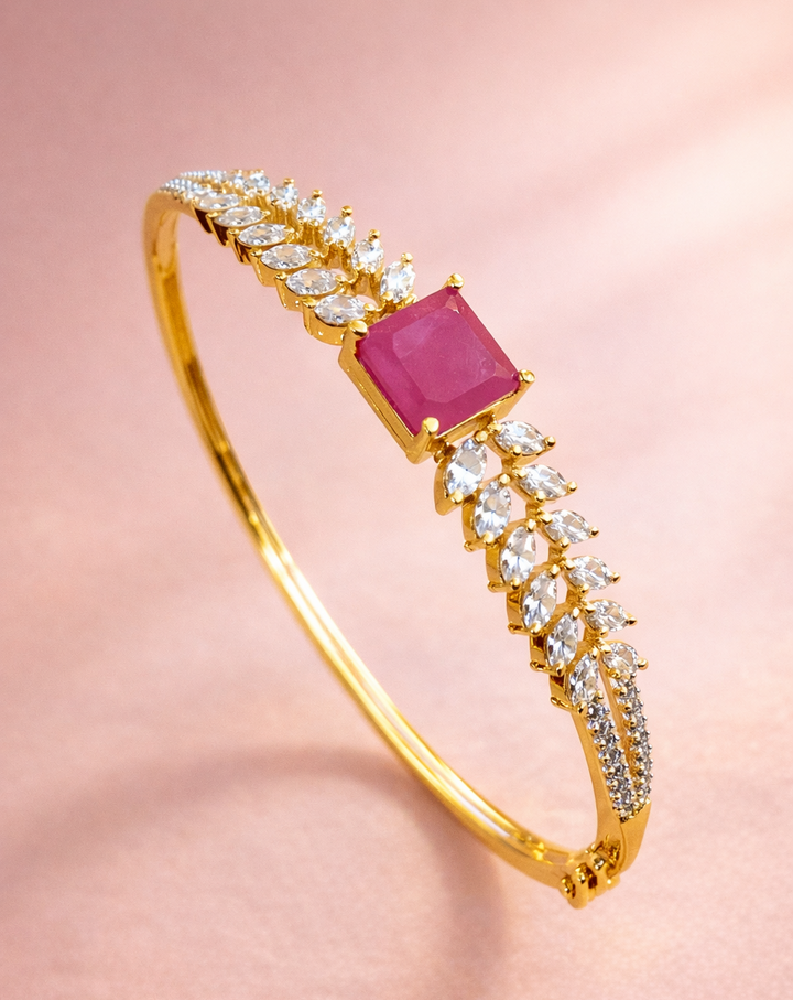 Gold bracelet with a pink gemstone and diamond accents on a pink background