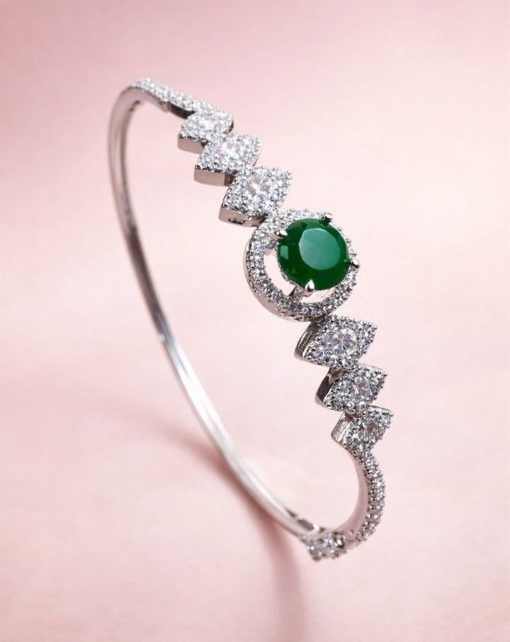 Silver bracelet with a green gemstone on a pink background