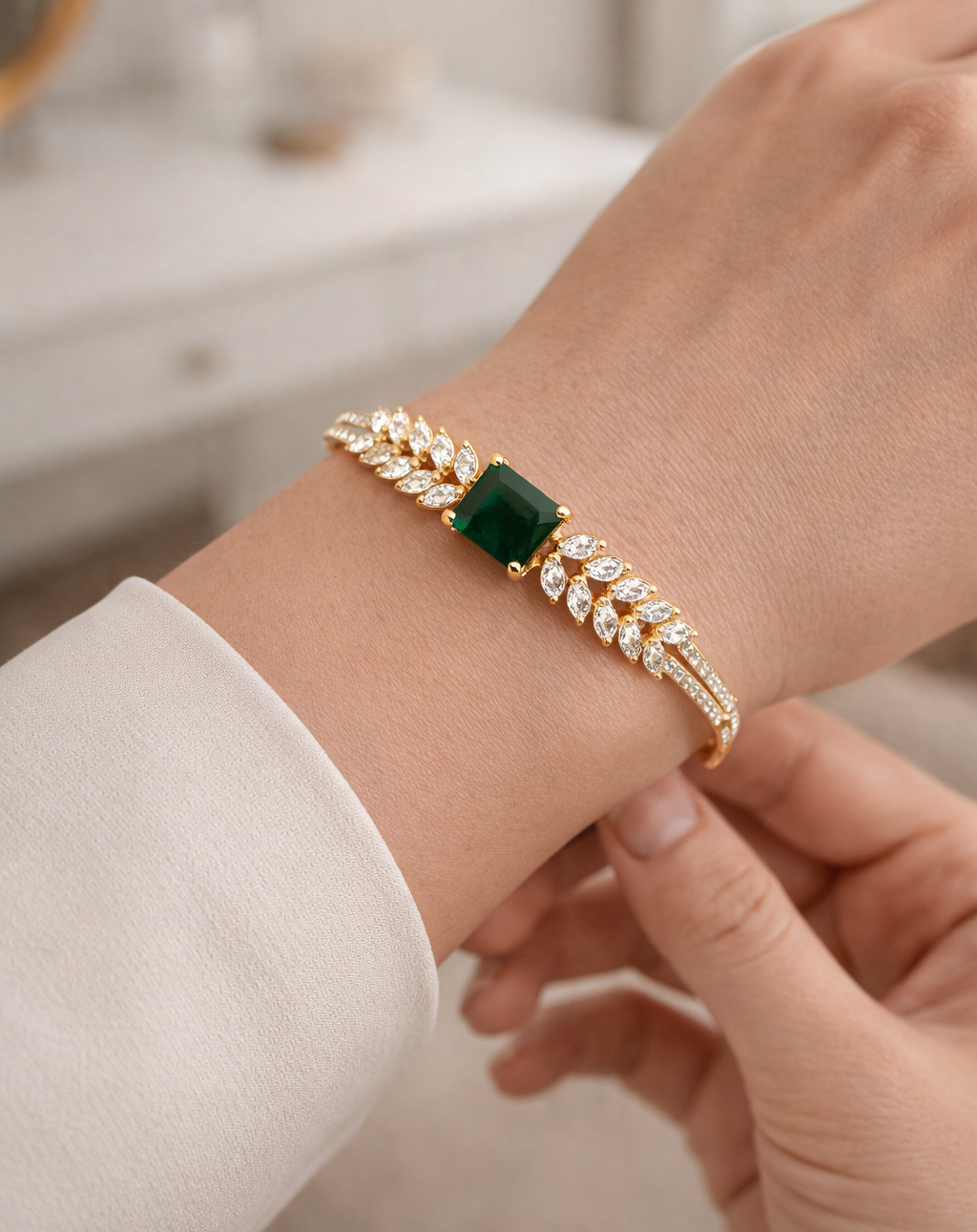 Gold bracelet with a green gemstone on a wrist against a neutral background