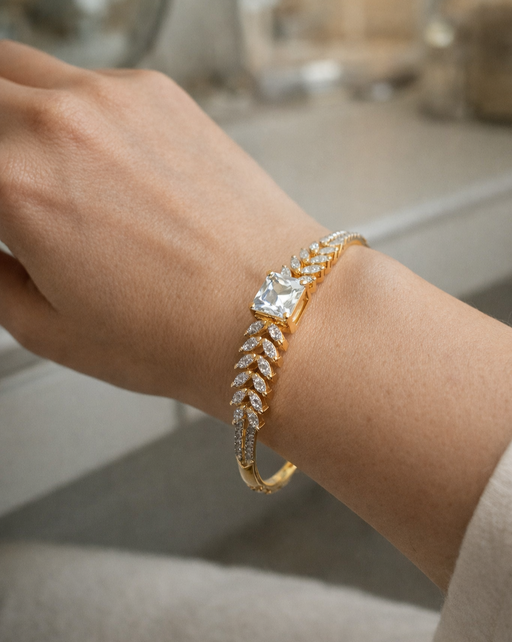 Gold bracelet with a large diamond on a wrist against a neutral background