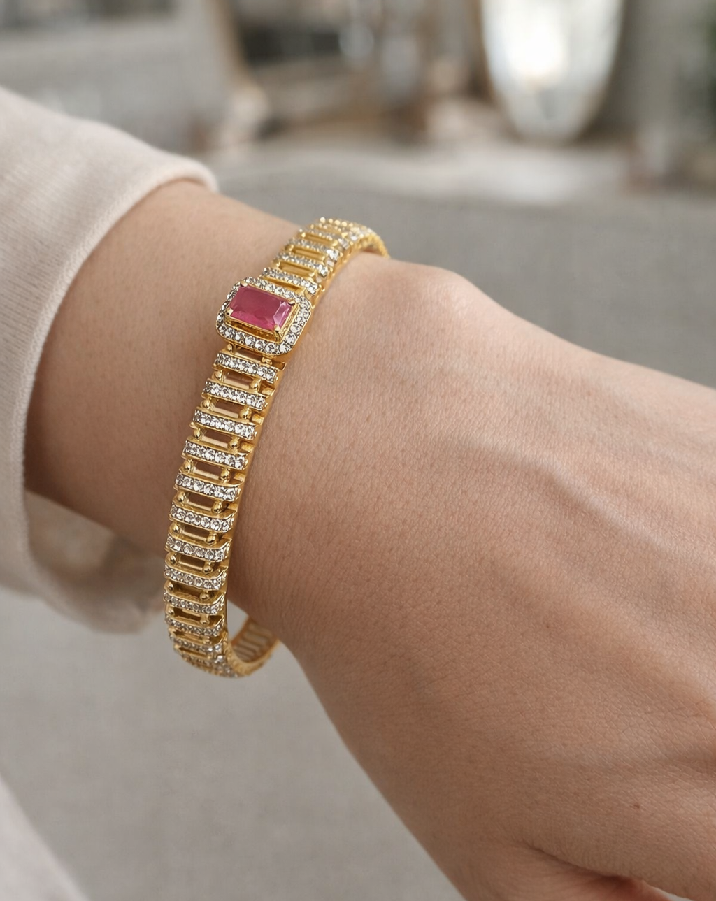 Gold bracelet with a pink gemstone on a wrist against a neutral background