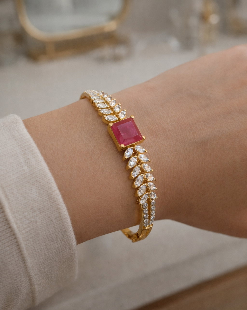 Gold bracelet with a red gemstone on a wrist against a neutral background
