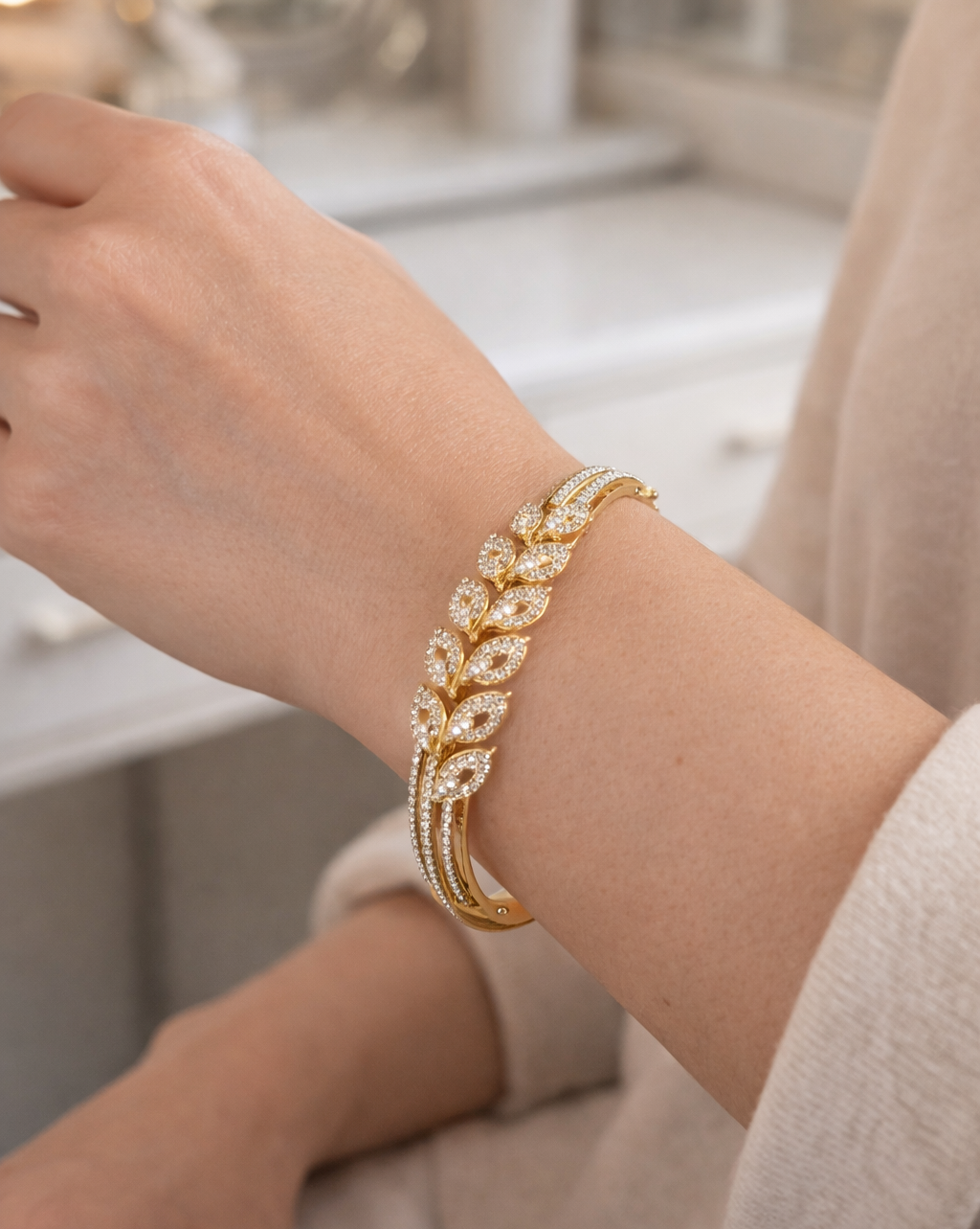 Gold bracelet with leaf design on a wrist against a neutral background