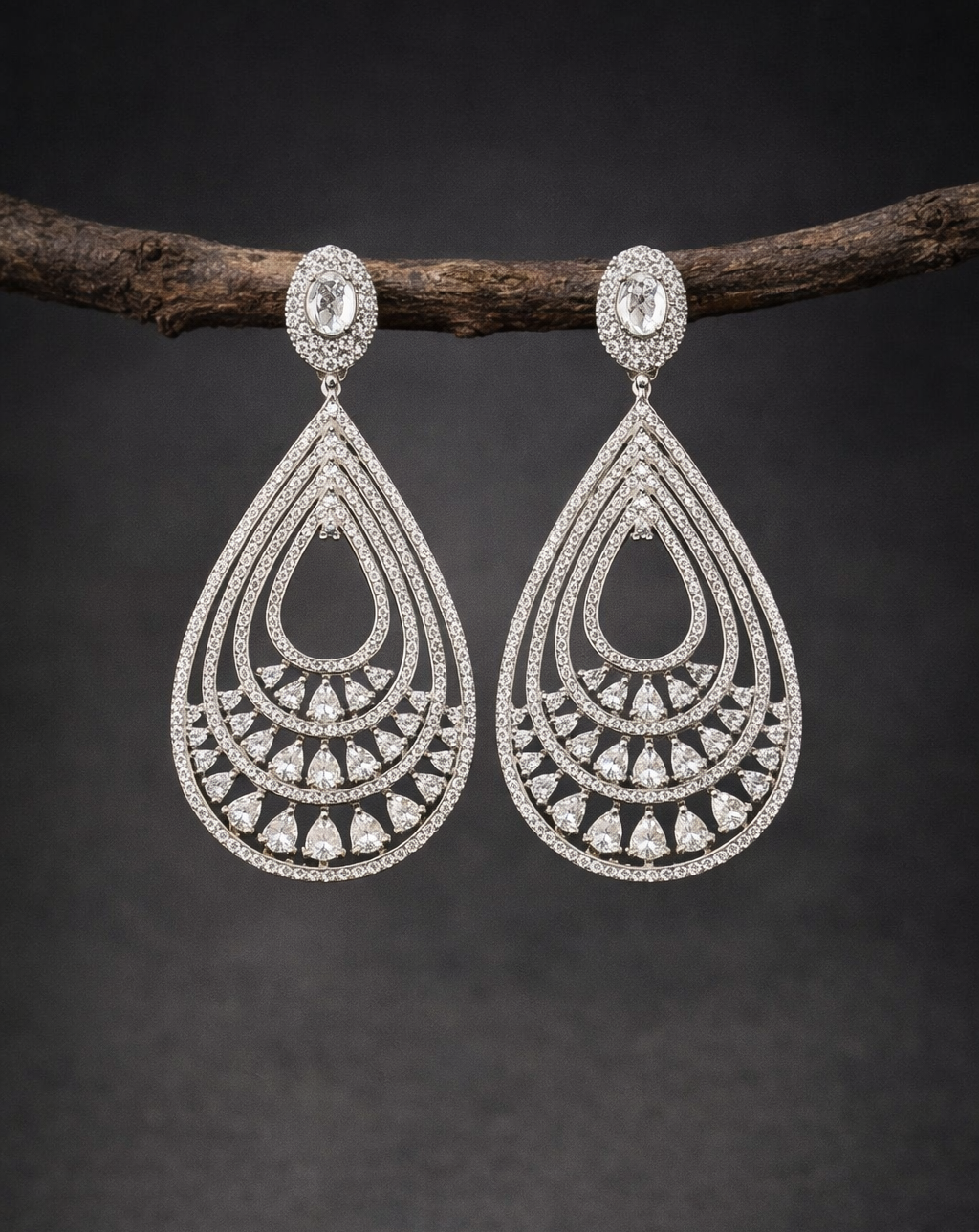 Pair of silver teardrop earrings with intricate designs on a dark background
