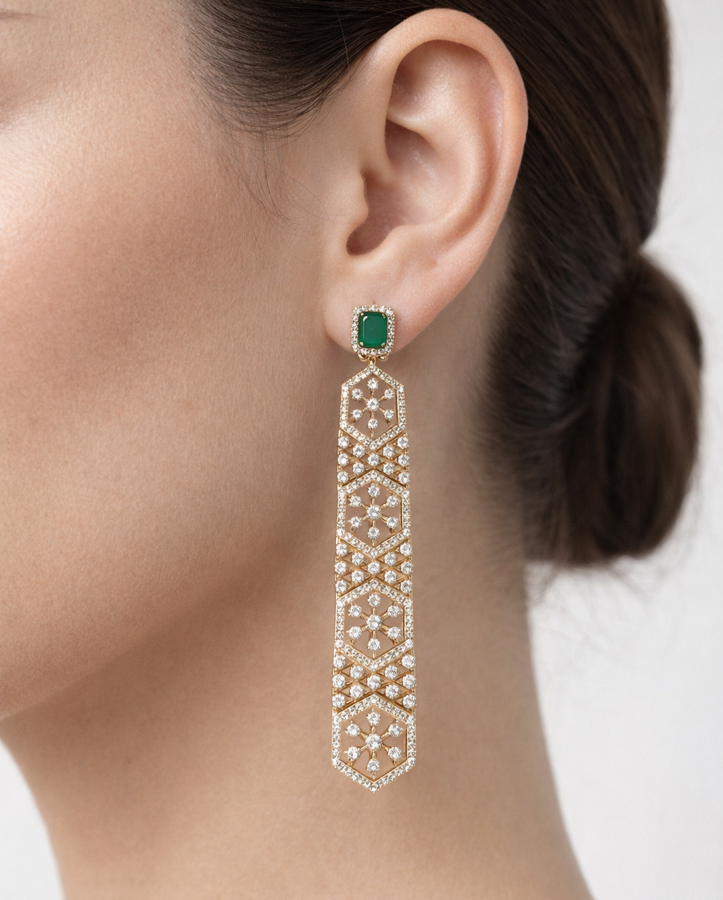Earring with green gemstone and diamond-like elements worn by a person.