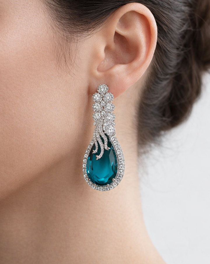 Close-up of a person wearing a blue teardrop earring with intricate detailing.