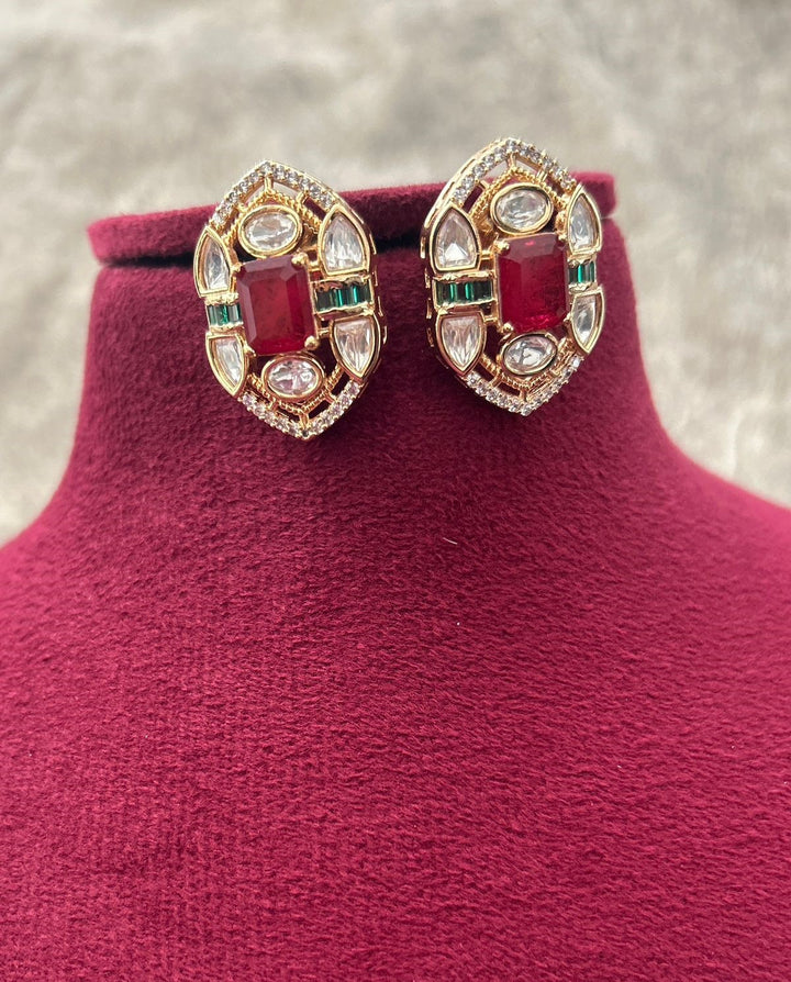 Pair of ornate earrings with red gemstones on a pink stand.