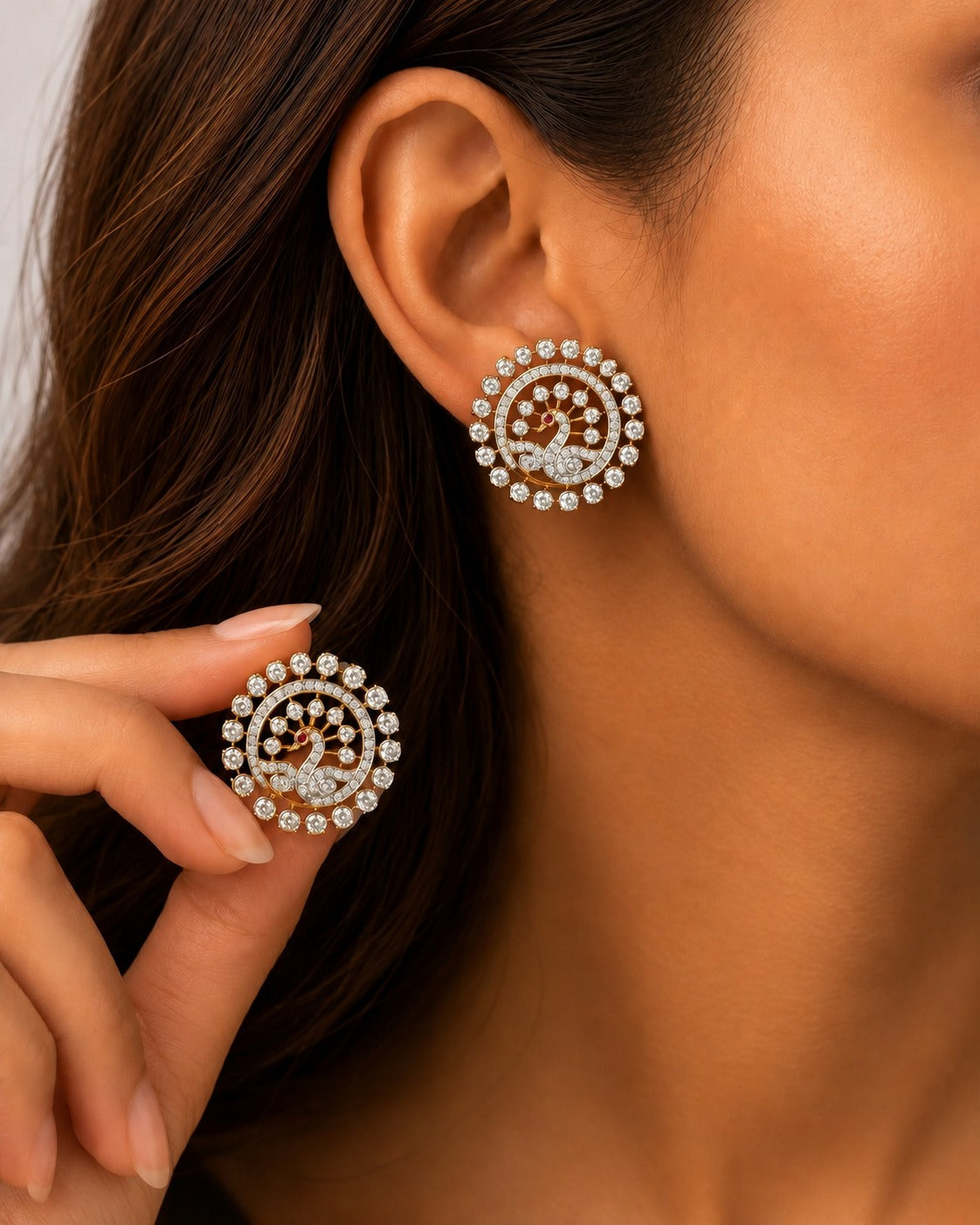 A close-up lifestyle shot of a model wearing a pair of circular gold and crystal earrings, with one earring shown on her ear and the other held near her cheek.