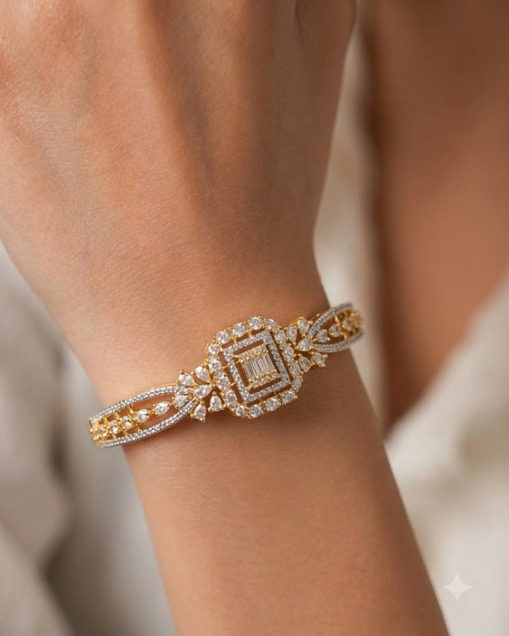 A close-up of a delicate gold and white gold cuff bracelet with pavé-set diamonds, worn on a person's wrist.