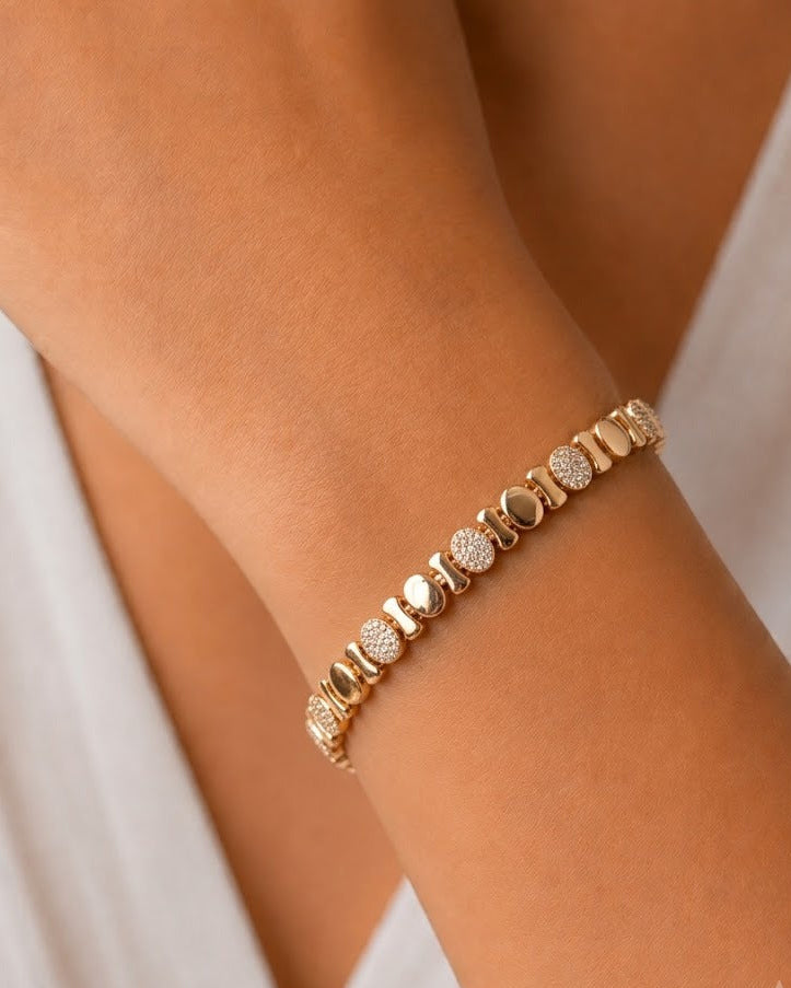 A close-up of a delicate gold bracelet with alternating polished round beads and textured pavé round beads, worn on a woman's wrist.