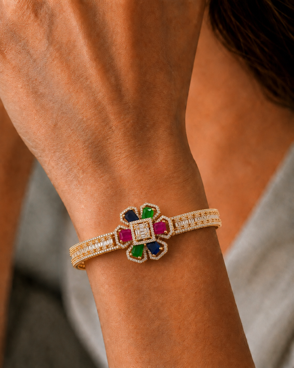 A close-up of a gold-toned bangle bracelet with a colorful floral center and pavé-set stones, worn on a person's wrist.