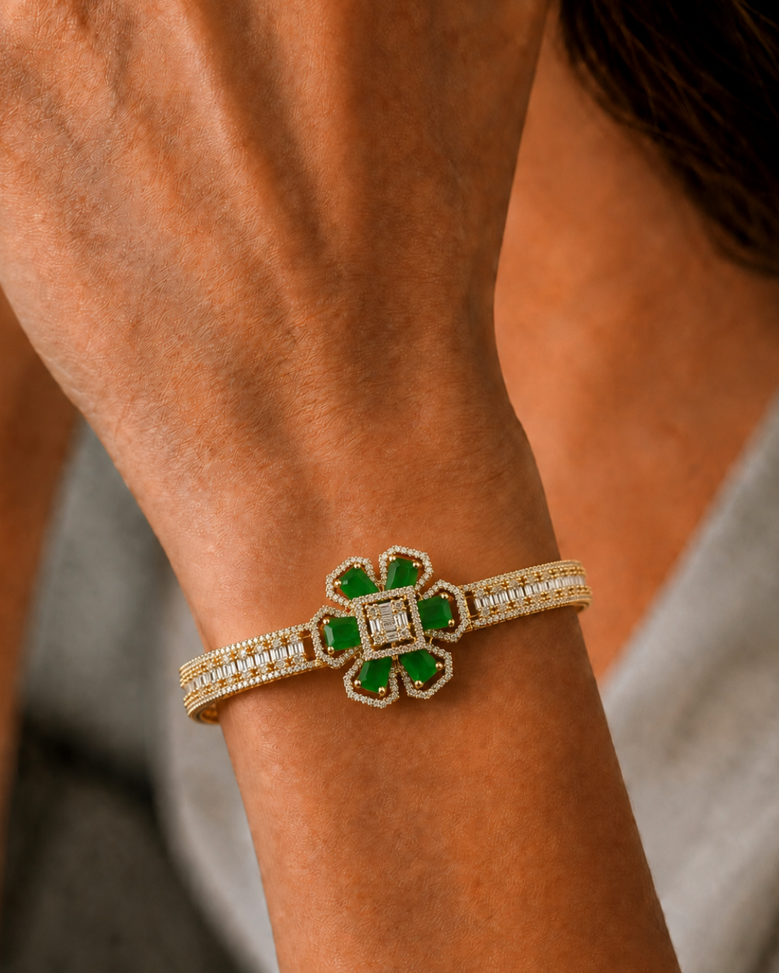 A close-up of a gold-toned bracelet with green emerald-cut stones and pavé-set clear stones, worn on a person's wrist.