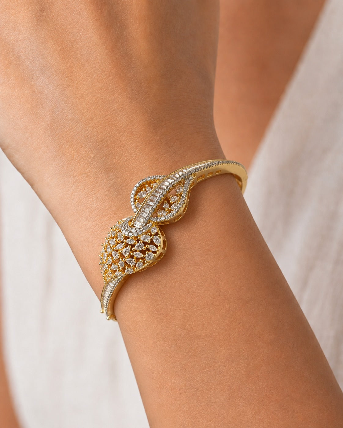 A close-up of a gold and diamond cuff bracelet worn on a person's wrist, set against a soft, light beige background.