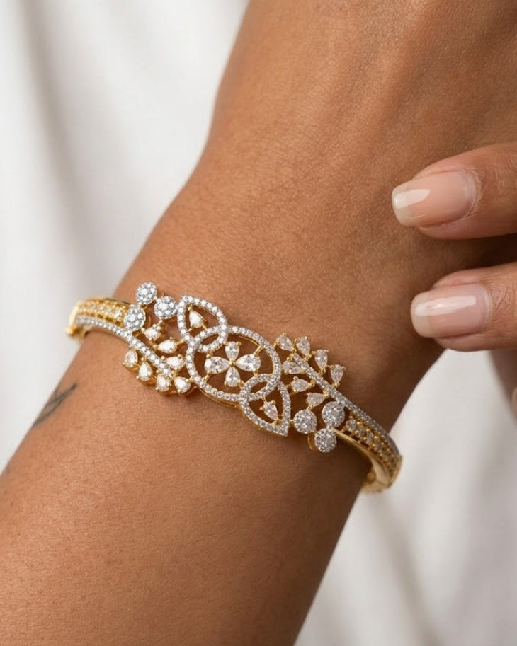 A close-up of a gold and white stone bracelet worn on a person's wrist, with fingers gently resting near the jewelry against a soft white background.