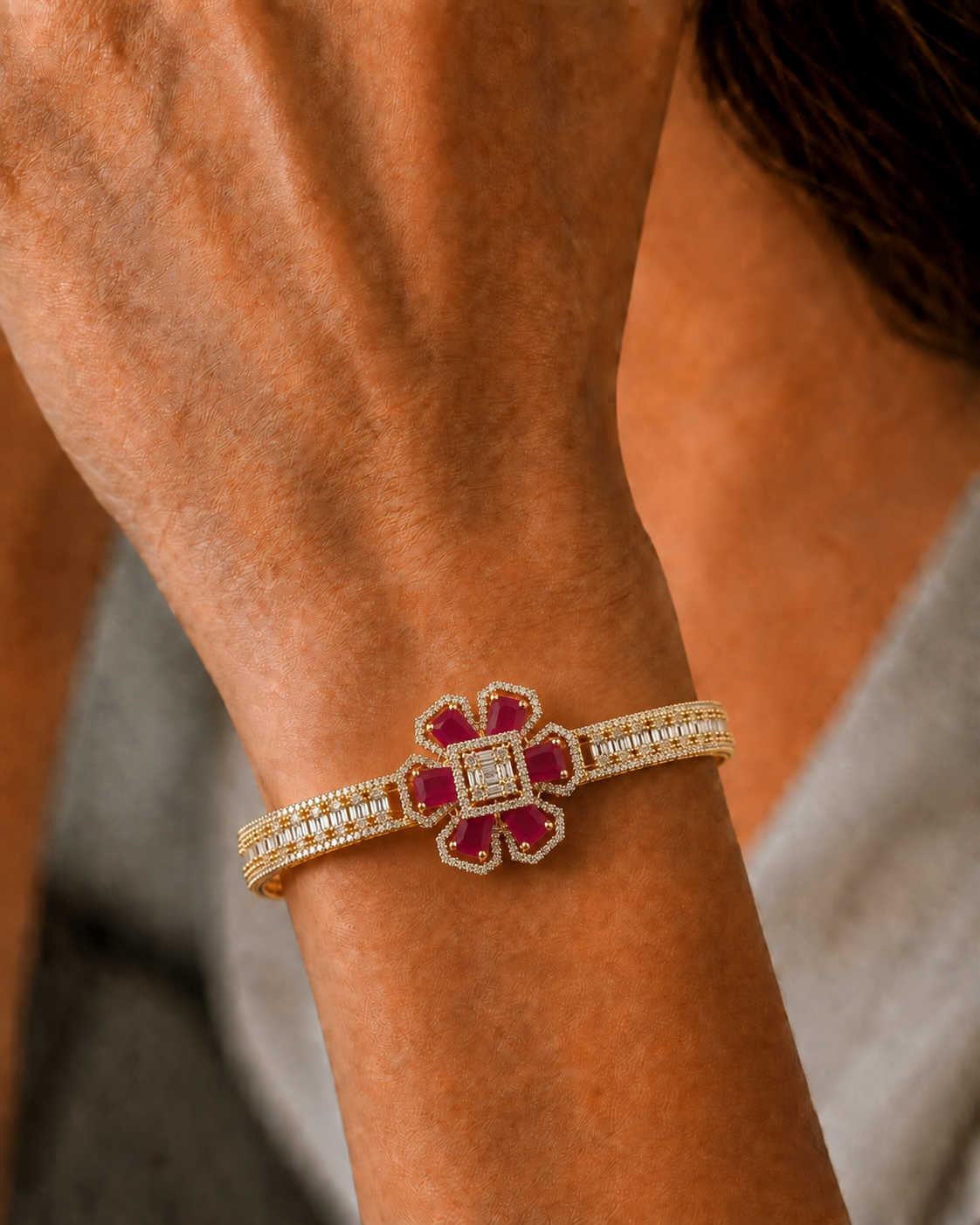 A close-up of a gold bracelet with a flower-shaped ruby and diamond centerpiece, worn on a person's wrist.