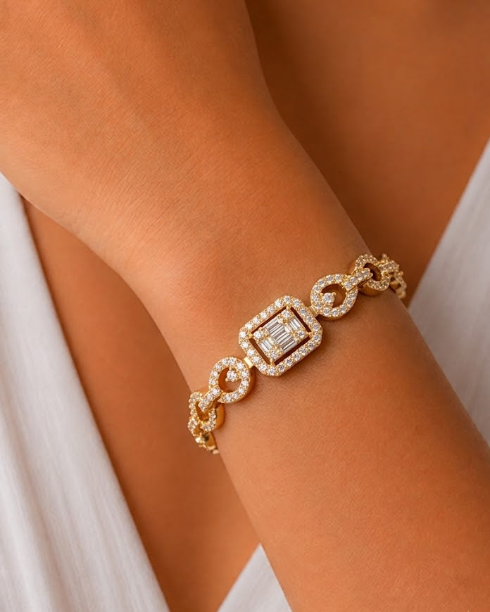 A close-up of a gold chain bracelet with diamond accents worn on a woman's wrist, paired with a white sleeveless dress.
