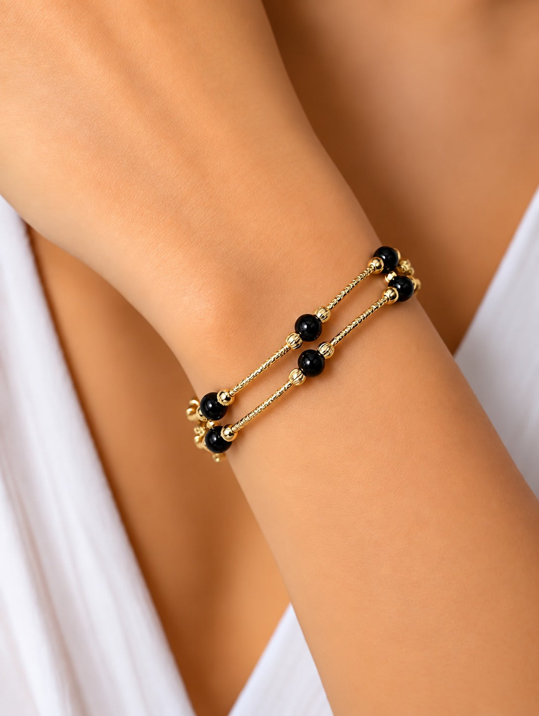 A close-up of a gold double-strand chain bracelet with small black beads, worn on a person's wrist.