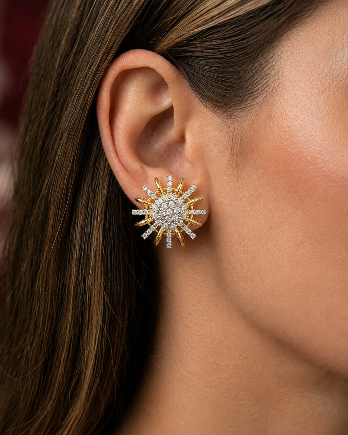 A close-up of a model's ear wearing a gold and white stone sunburst stud earring.