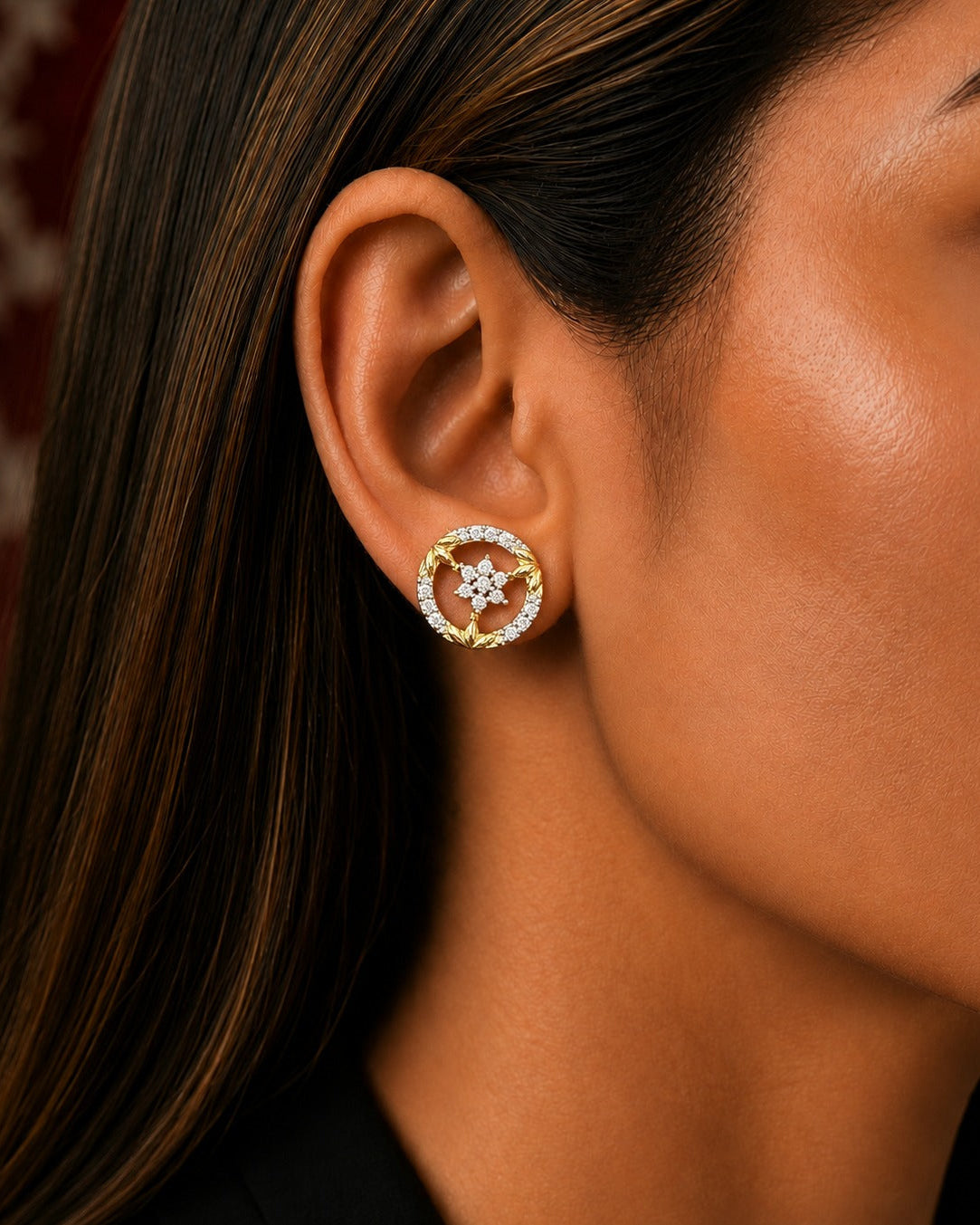 A close-up of a model's ear wearing a gold and white stone stud earring with a central floral star motif.