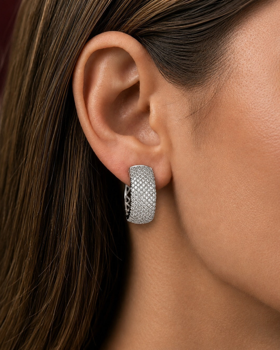 A close-up of a model's ear wearing a textured silver hoop earring with pavé-set stones.
