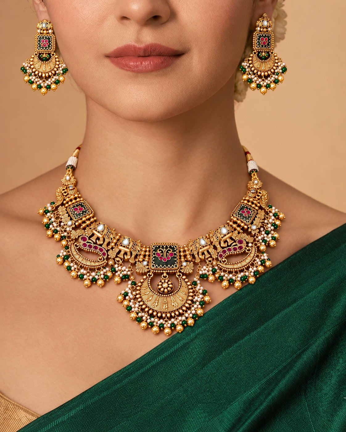 A close-up of a model wearing an ornate gold-toned traditional necklace with matching dangling earrings, styled with a deep green saree against a warm beige background.