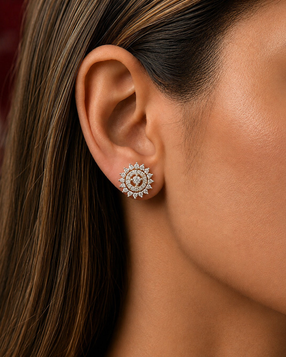 A close-up of a woman's ear wearing a round, intricate silver-toned stud earring with small clear stones.