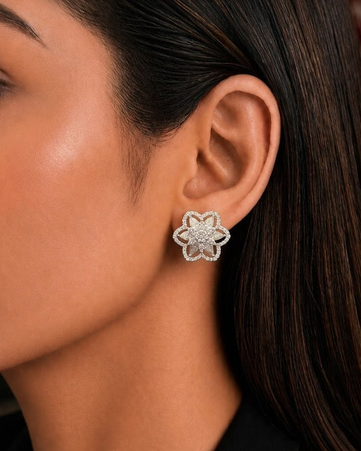 A close-up of a woman's ear wearing a small flower-shaped stud earring with a silver-toned metal border and clear stones.