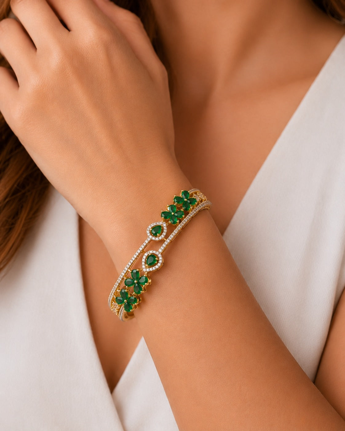 A close-up of a woman's wrist wearing a gold-toned double-strand bracelet adorned with green emerald-cut stones and a border of small clear pavé stones.