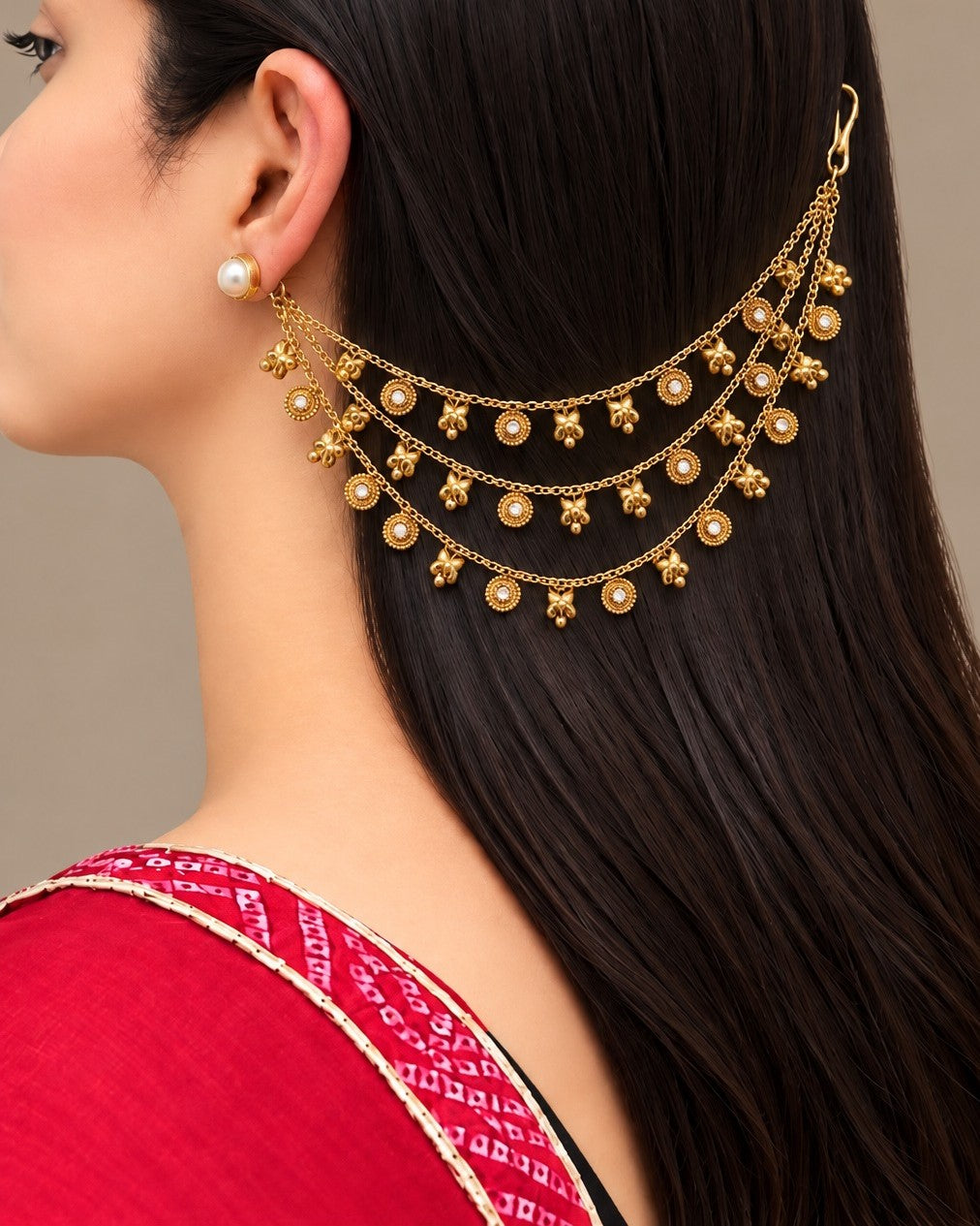 A close-up of a woman wearing a gold-toned multi-strand hair chain with pearl-like beads, shown from the side against a neutral beige background.