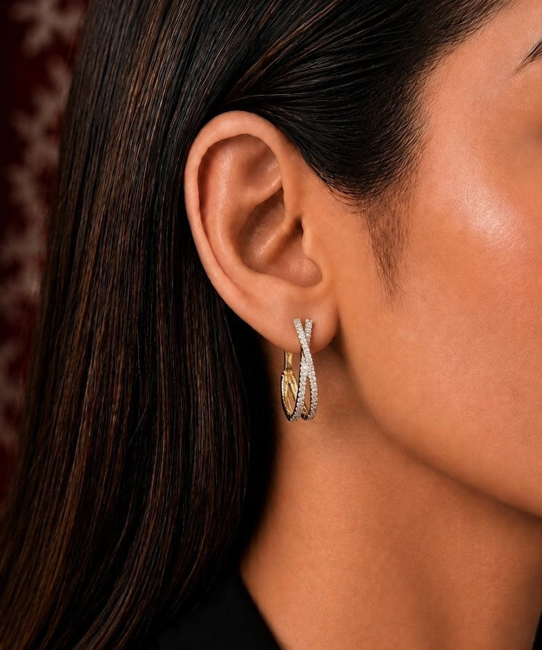 A close-up side profile of a woman wearing a delicate gold and silver twisted hoop earring with a small heart charm.