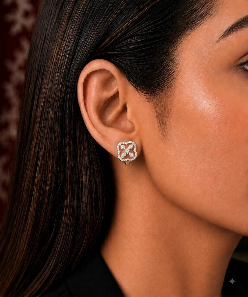 A close-up side profile of a woman wearing a small floral stud earring in a yellow gold setting with clear stones.