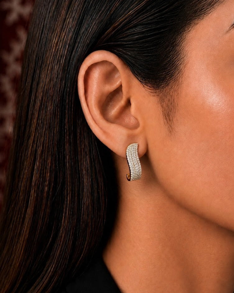 A close-up side profile of a woman wearing a small curved hoop earring set with clear stones in a silver-toned metal.