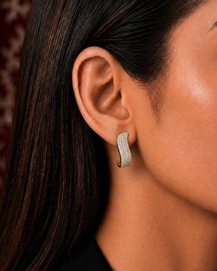 A close-up side profile of a woman wearing a small curved hoop earring set with clear stones in a silver-toned metal.