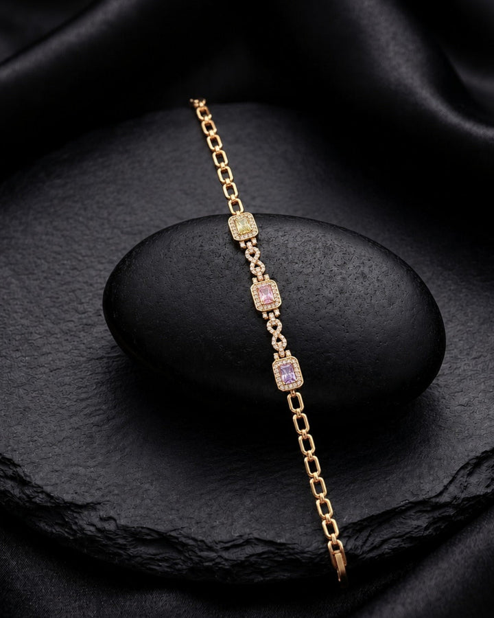 A delicate gold chain bracelet with three rectangular purple gemstone accents, displayed on a black stone pedestal against a draped black satin background.
