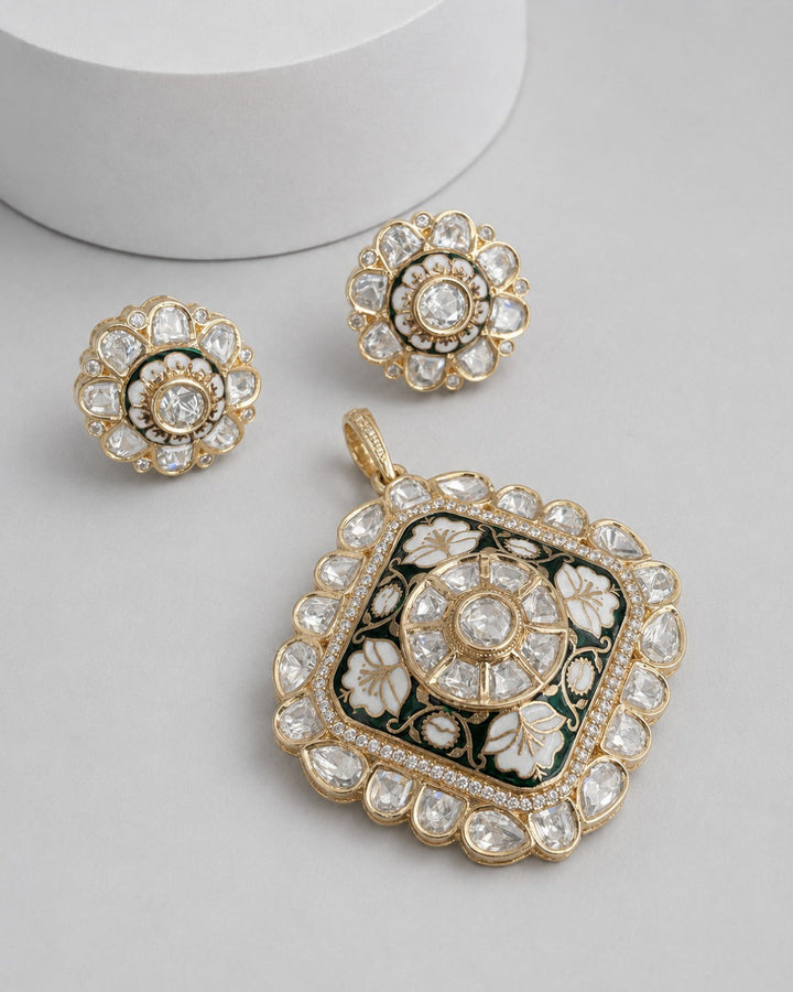 A gold-plated jewelry set featuring a large square pendant and two matching round earrings, decorated with clear stones, white floral enamel, and dark green accents on a light gray background.