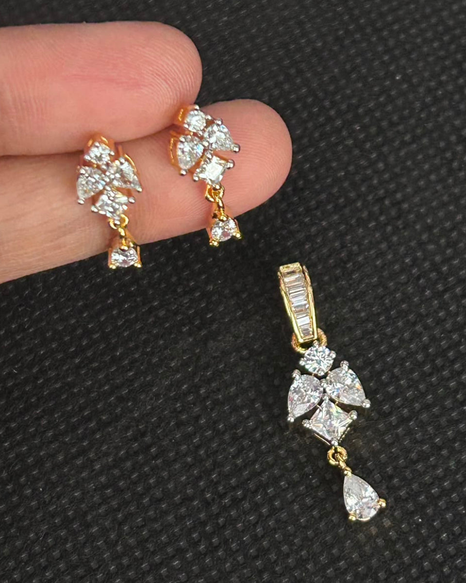 A pair of gold and crystal drop earrings held between fingers against a textured black background, with a matching single earring shown below.