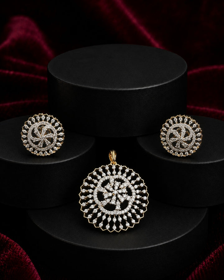 A gold-toned jewelry set featuring a round pendant and matching stud earrings with intricate circular patterns set with clear stones, displayed on black cylindrical pedestals against a dark red velvet background.