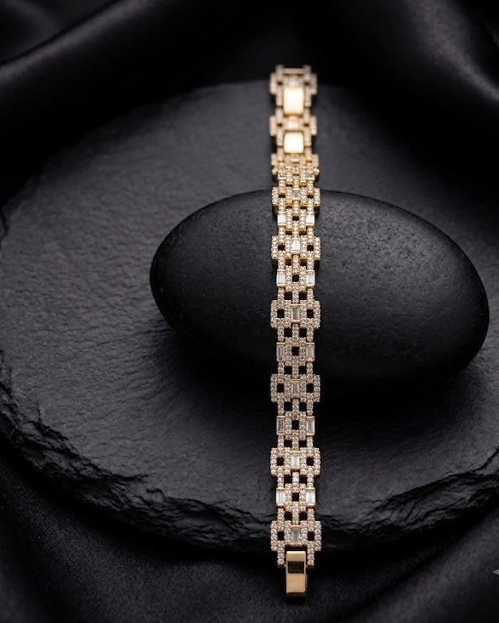 A gold-toned link bracelet with pavé-set clear stones, displayed vertically on a dark stone pedestal against a black satin fabric background.