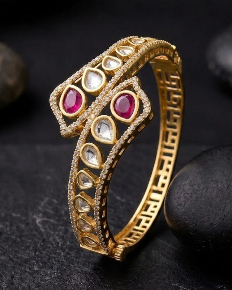 A gold snake-shaped with red and clear gemstones, displayed on a dark textured surface with smooth black stones.