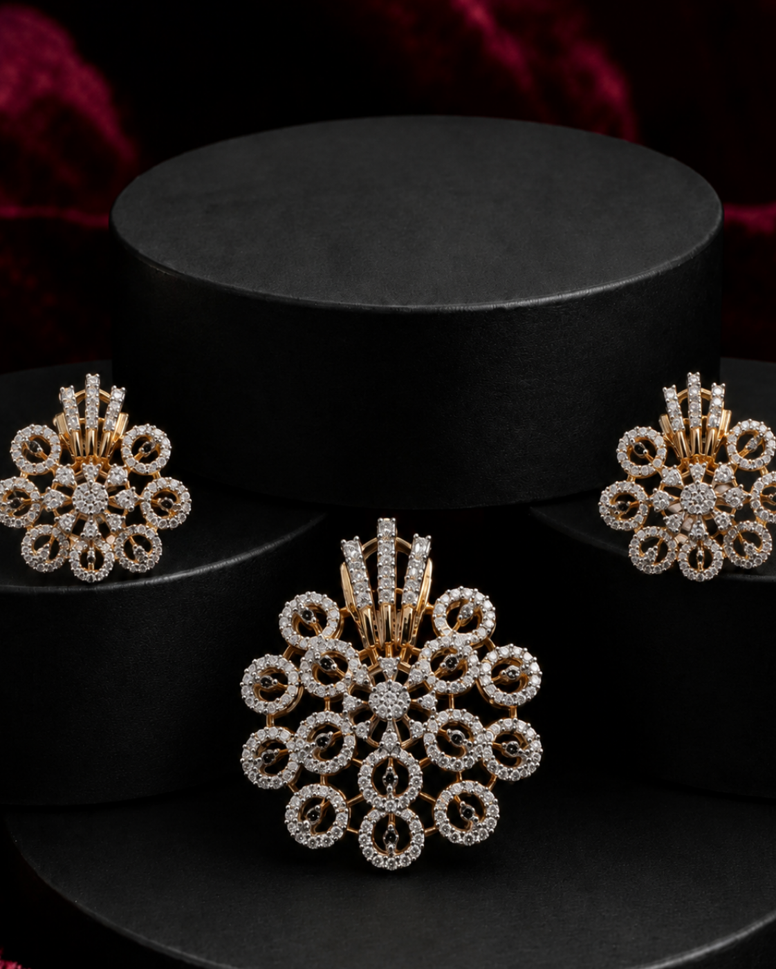 A gold and diamond jewelry set featuring a large floral pendant, matching stud earrings, and a small matching hair pin, displayed on a black cylindrical pedestal against a dark background with red fabric.