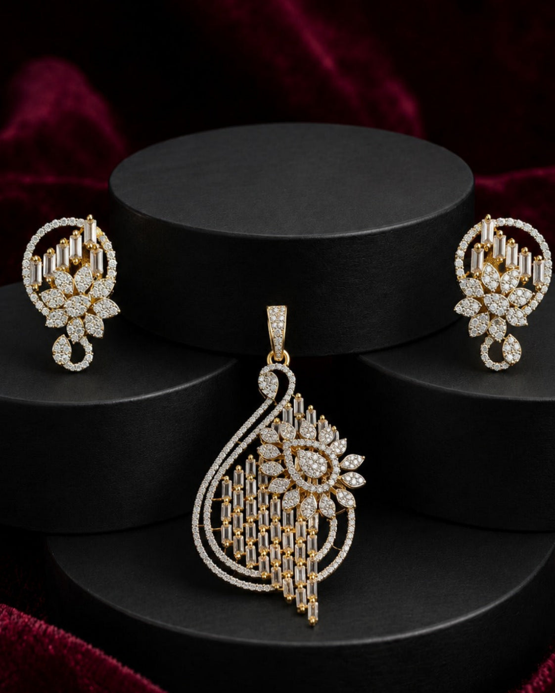 A gold and diamond jewelry set featuring a large teardrop pendant, matching earrings, and a small nose stud, displayed on black cylindrical pedestals against a dark red velvet background.