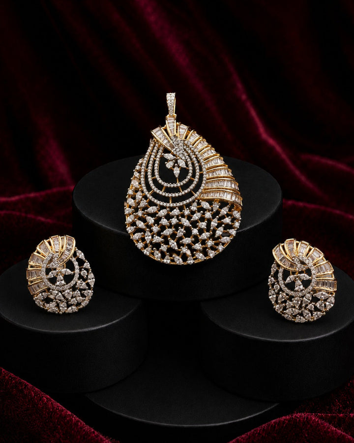 A gold and diamond jewelry set featuring a teardrop-shaped pendant, matching earrings, and a small nose stud, displayed on black cylindrical pedestals against a dark red velvet background.