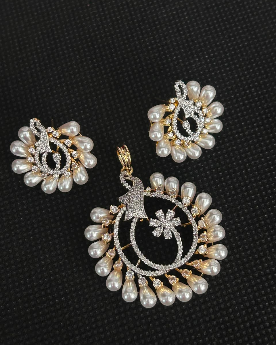 A gold and silver jewelry set featuring a large pendant and matching earrings decorated with white faux pearls and sparkling clear stones, displayed on a textured black background.
