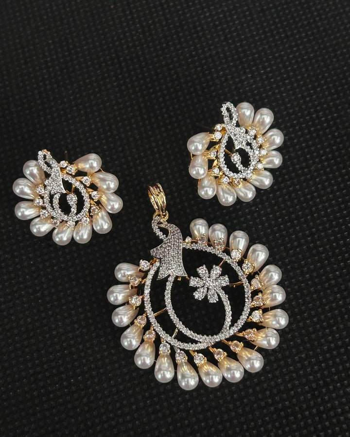 A gold and silver jewelry set featuring a large pendant and matching earrings decorated with white faux pearls and sparkling clear stones, displayed on a textured black background.