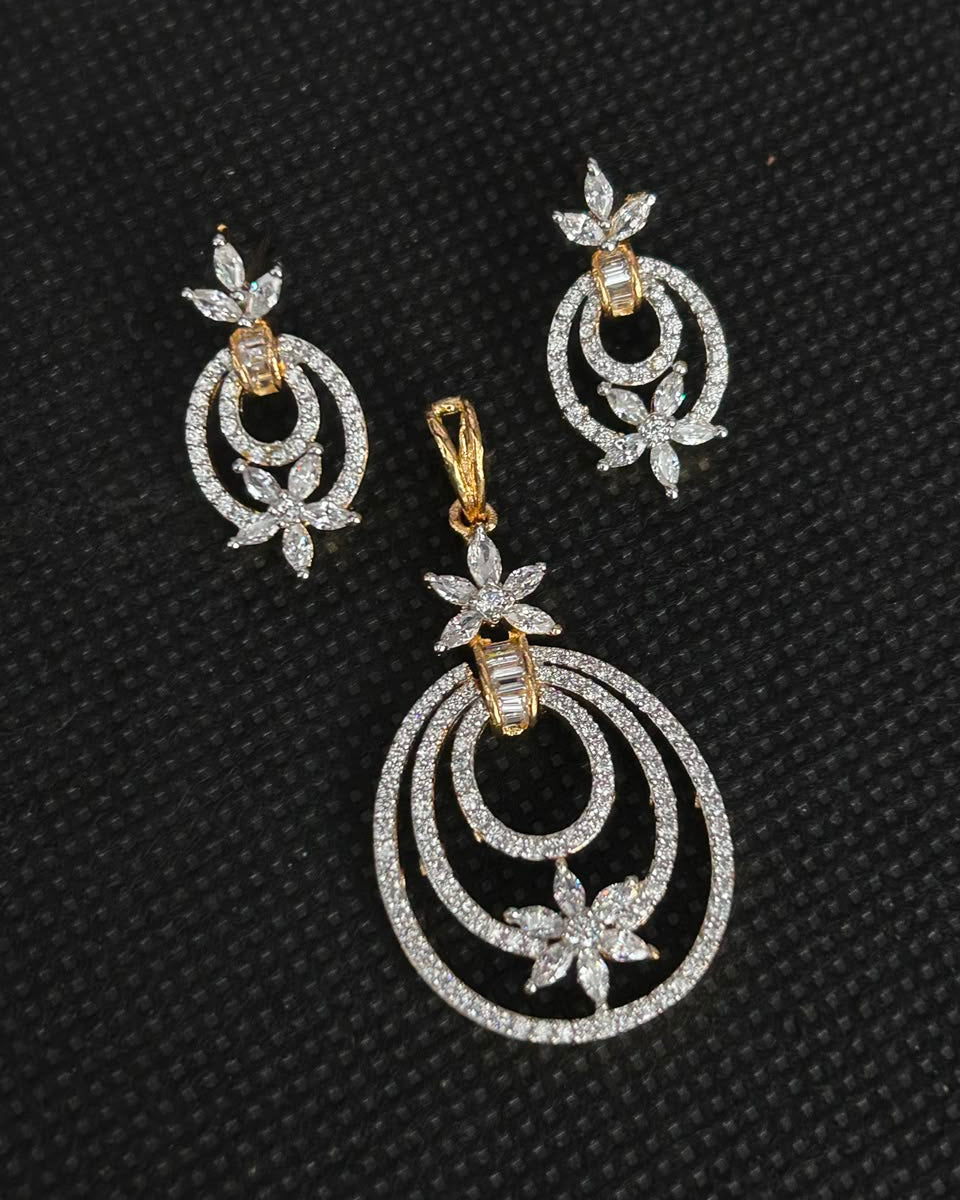 A gold and silver-tone jewelry set featuring a large circular pendant and matching earrings, embellished with clear stones on a textured black background.
