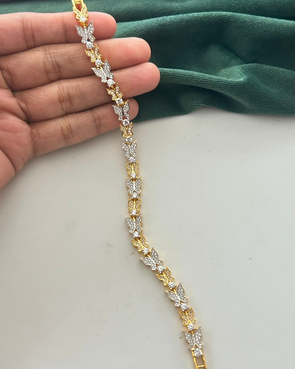 A gold and silver-toned butterfly link bracelet held in a hand against a white surface with a dark green fabric backdrop.