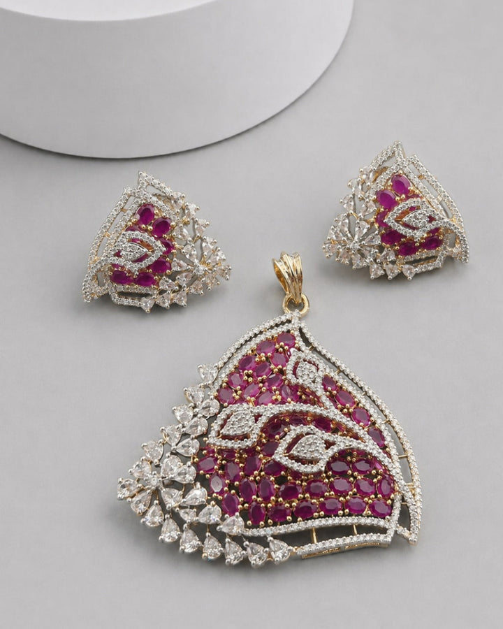 A gold and silver jewelry set featuring a large scalloped pendant, matching triangle earrings, and a small box, all embellished with deep pinkish-red stones and clear crystals on a light gray background.