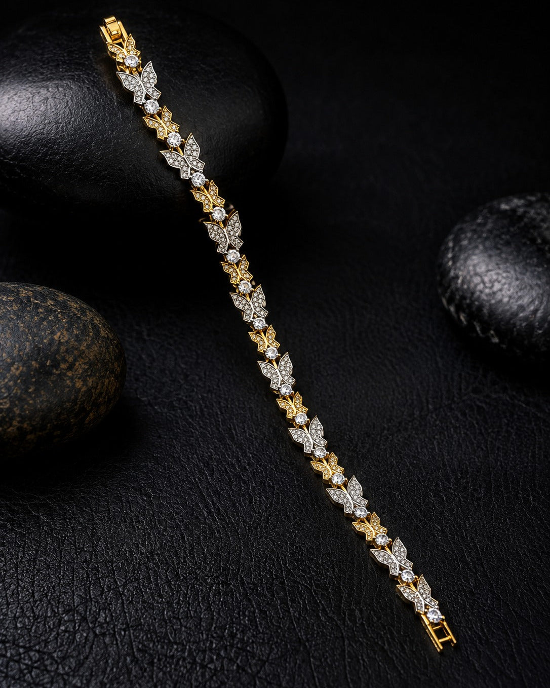 A gold and white crystal leaf-link bracelet displayed diagonally on a textured black surface with dark decorative stones.
